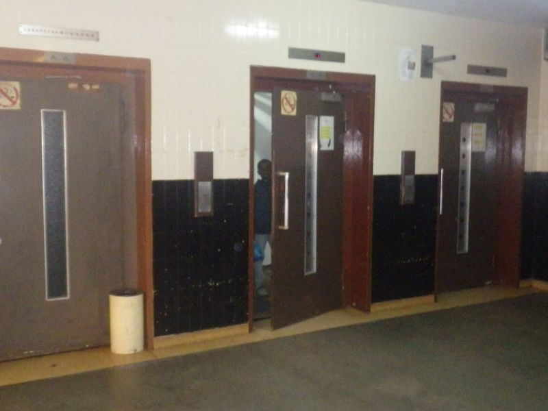 A communal hallway area featuring three elevator access points with dated wall tiling and finishes.