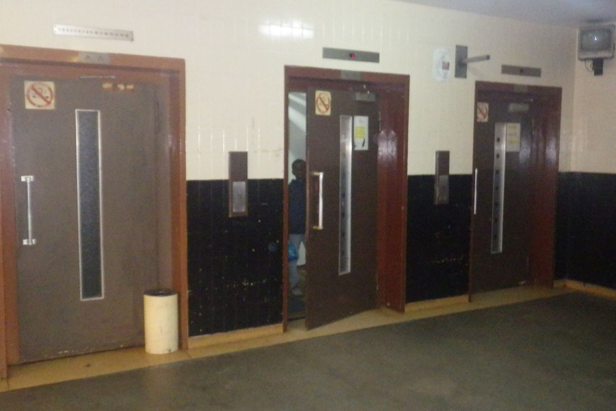 A communal hallway area featuring three elevator access points with dated wall tiling and finishes.