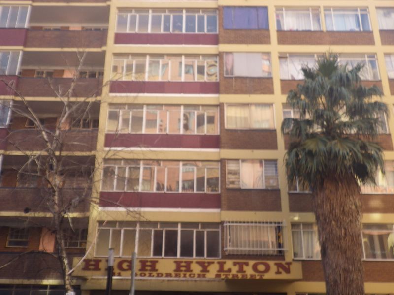 Front elevation of the High Hylton apartment building, featuring a multi-story brick facade with numerous windows and established palm trees.