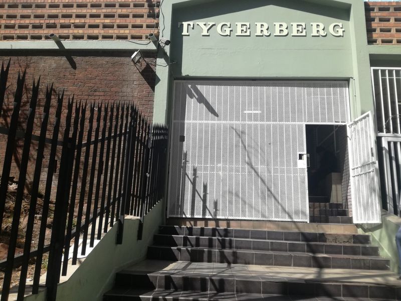 Front entrance of the Tygerberg building featuring a security gate, tiled staircase, and brick facade.