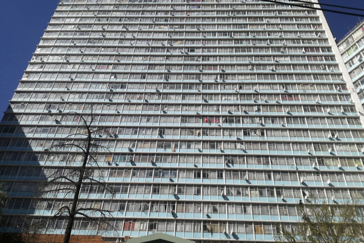 A low-angle view of the Tygerberg high-rise apartment building, showcasing its multi-story facade with numerous windows and balcony structures.