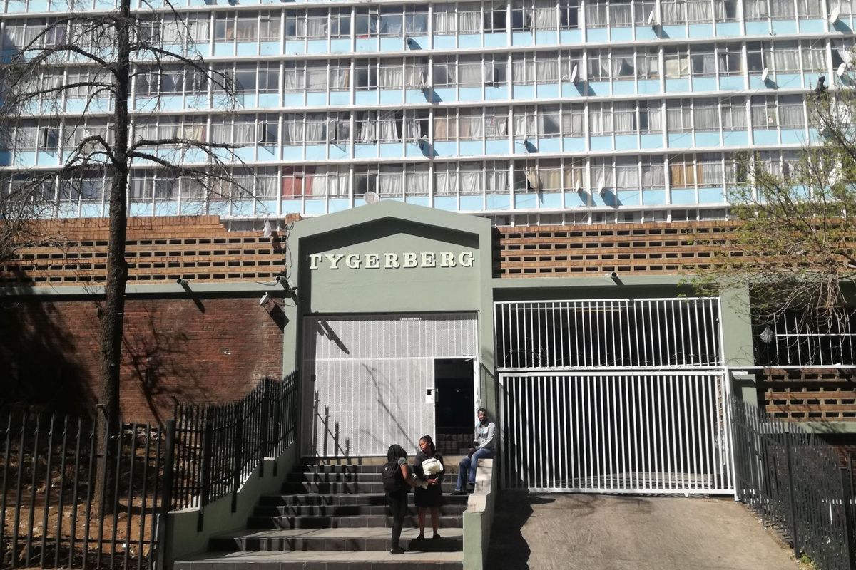 Front entrance view of the Tygerberg apartment complex, featuring a secure gated driveway, concrete staircase, and multi-story residential facade.