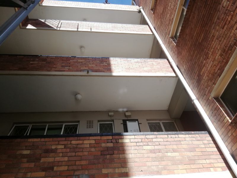 Upward view of the rear brick facade of a multi-story flat complex, featuring stacked balconies and external drainage infrastructure.