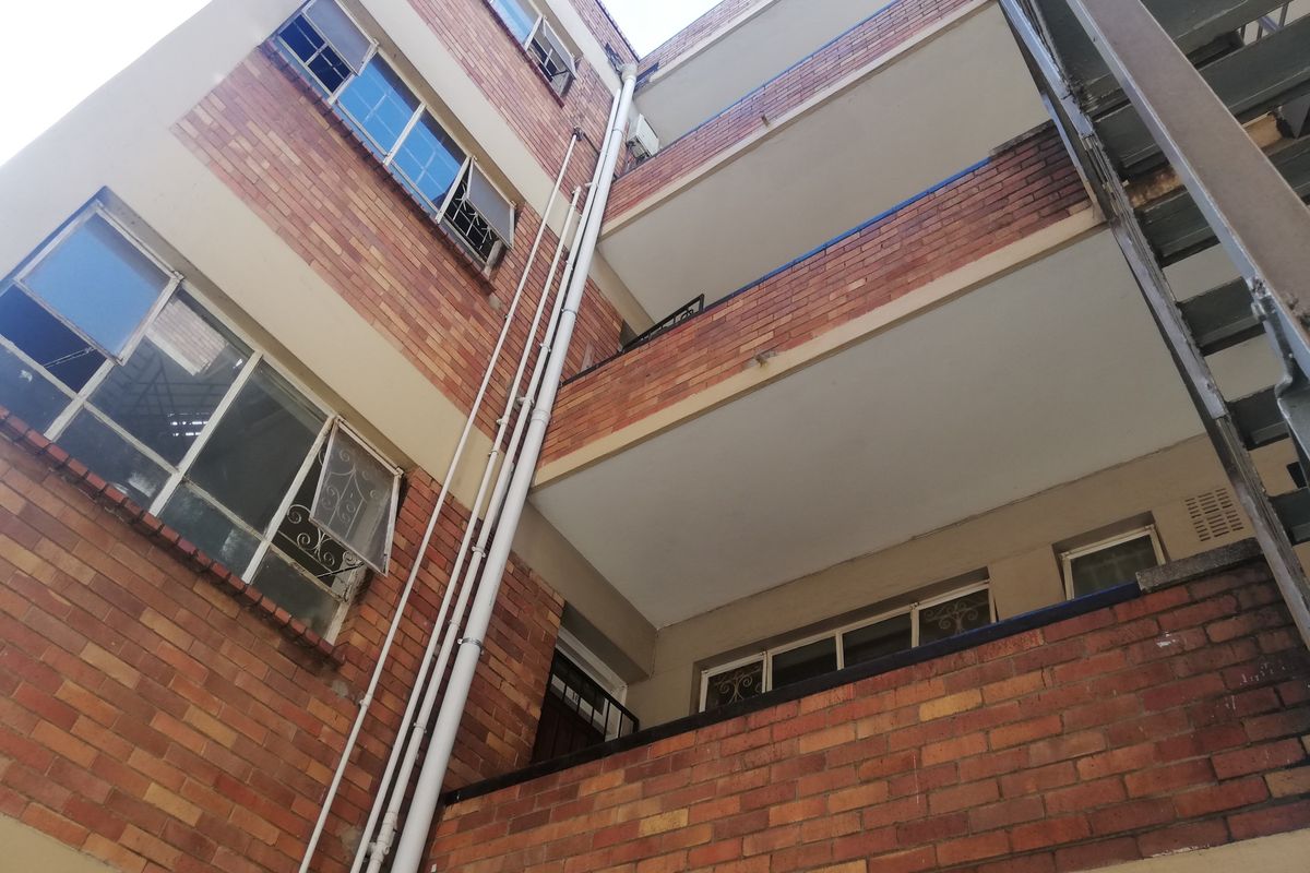 Low-angle view of a multi-story brick apartment building featuring external balconies, steel-framed windows, and an external metal staircase.
