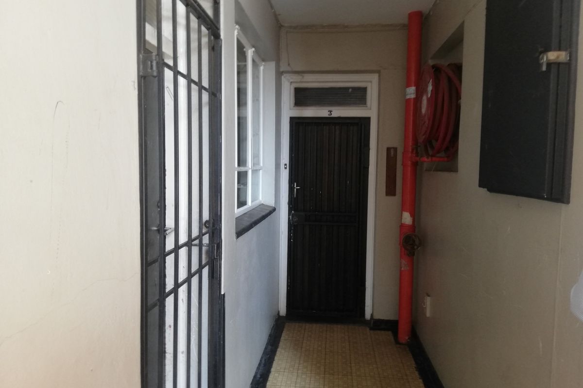 A functional apartment hallway featuring a security gate, fire safety equipment, and tiled flooring leading to the unit entrance.