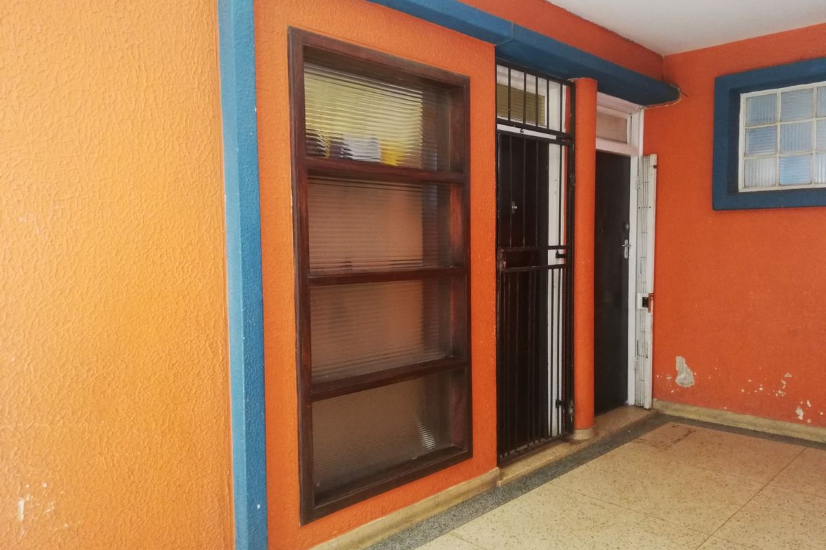 A covered patio area featuring textured orange walls, a security gate, and a large fluted glass window with tiled flooring.