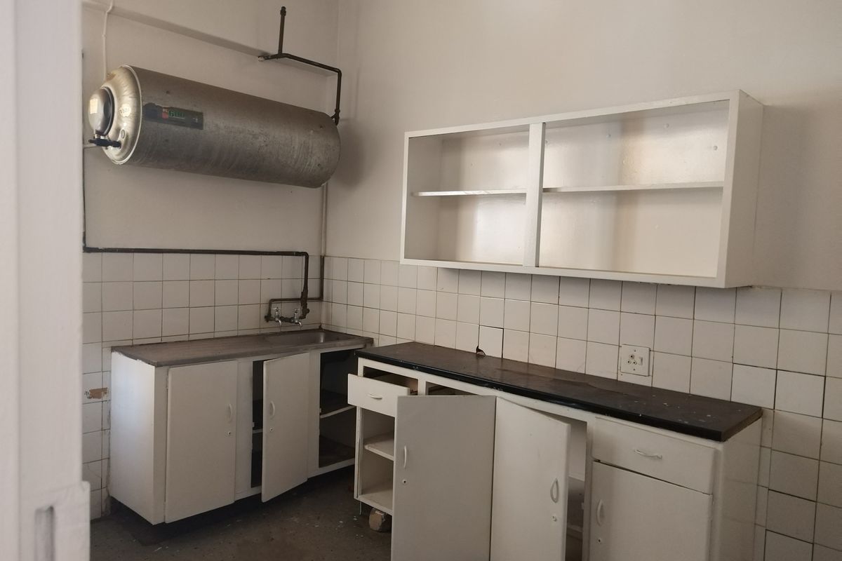 A dated scullery or utility area featuring built-in cabinetry, a stainless steel sink, and an exposed electric water heater.