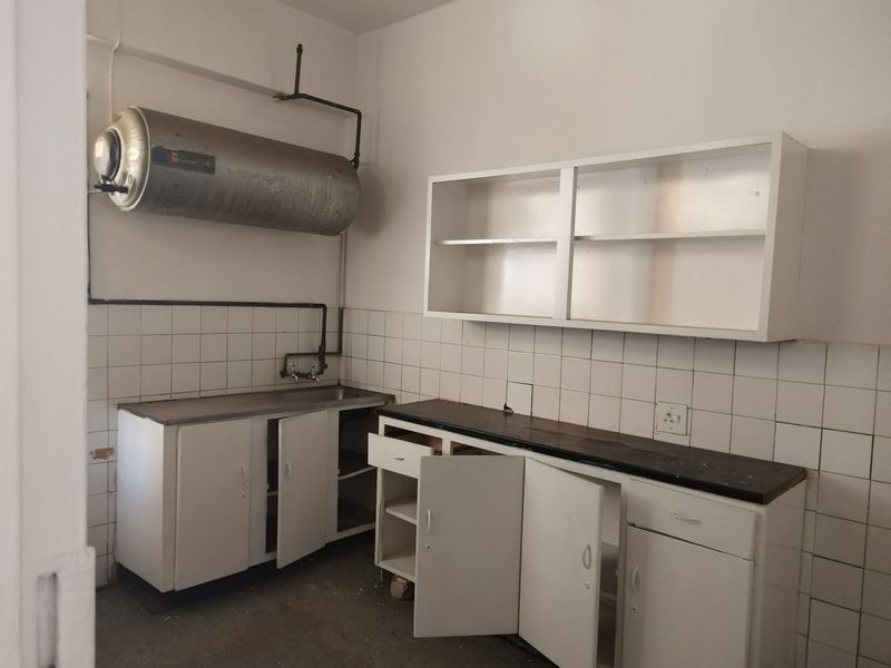 A dated scullery or utility area featuring built-in cabinetry, a stainless steel sink, and an exposed electric water heater.
