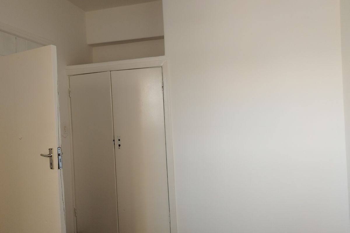 A simple, vacant bedroom featuring a built-in cupboard with white doors and neutral wall finishes.