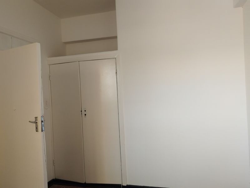 A simple, vacant bedroom featuring a built-in cupboard with white doors and neutral wall finishes.
