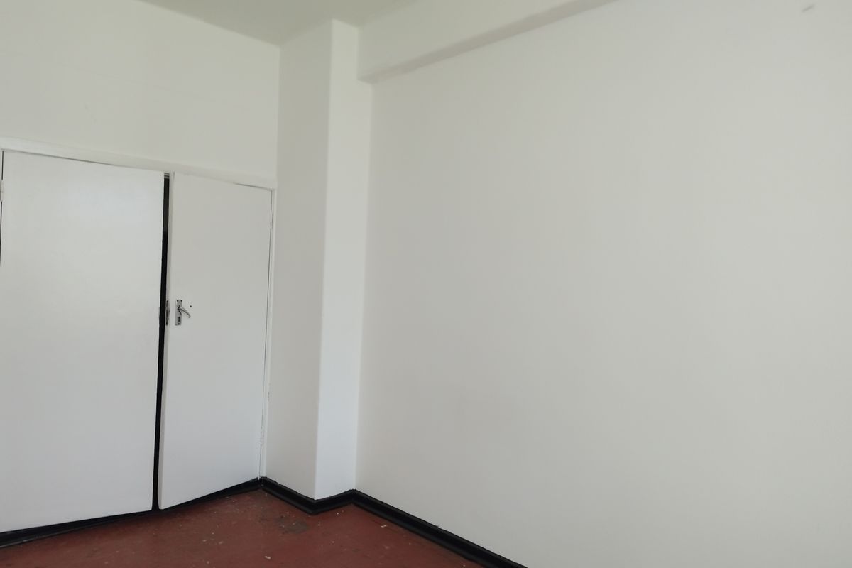 An empty bedroom featuring a built-in cupboard, white walls, and worn flooring, offering a blank canvas for renovation or interior design.