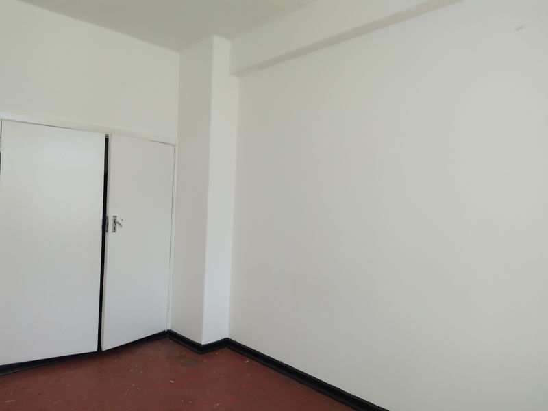 An empty bedroom featuring a built-in cupboard, white walls, and worn flooring, offering a blank canvas for renovation or interior design.