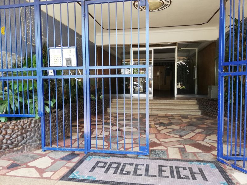 Secure building entrance featuring a blue metal security gate, mosaic tiled flooring with building name inlay, and glass entry doors.