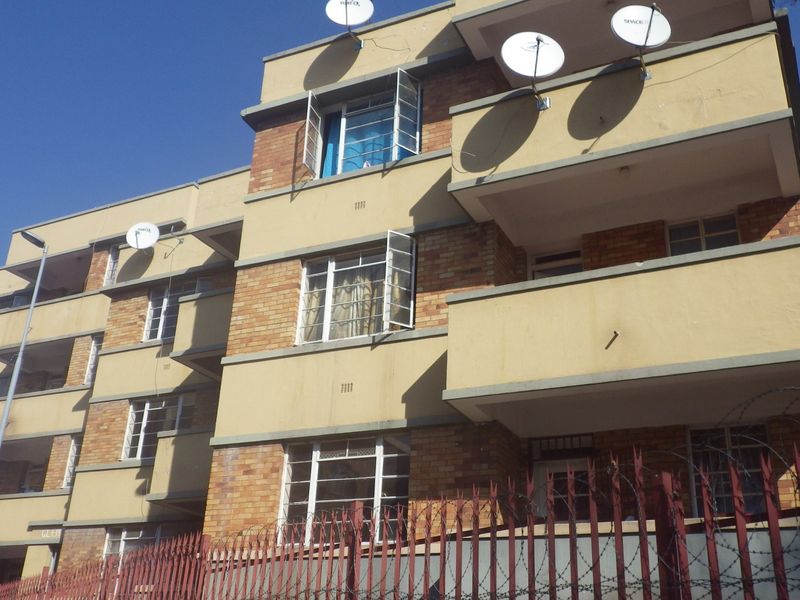 A multi-story apartment building featuring a brick and painted facade, private balconies, and secure perimeter fencing.