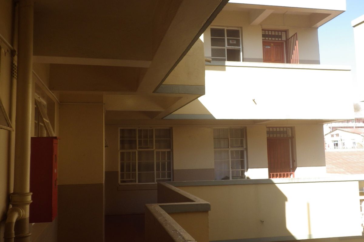 Exterior view of a multi-story flat complex featuring concrete walkways, external staircases, and fire safety equipment.