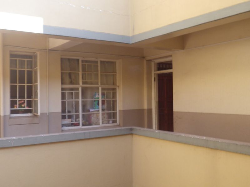 Exterior view of a flat complex corridor featuring concrete balustrades, timber doors, and window security bars.