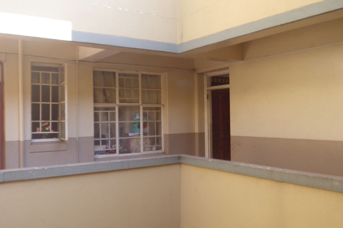 Exterior view of a flat complex corridor featuring concrete balustrades, timber doors, and window security bars.