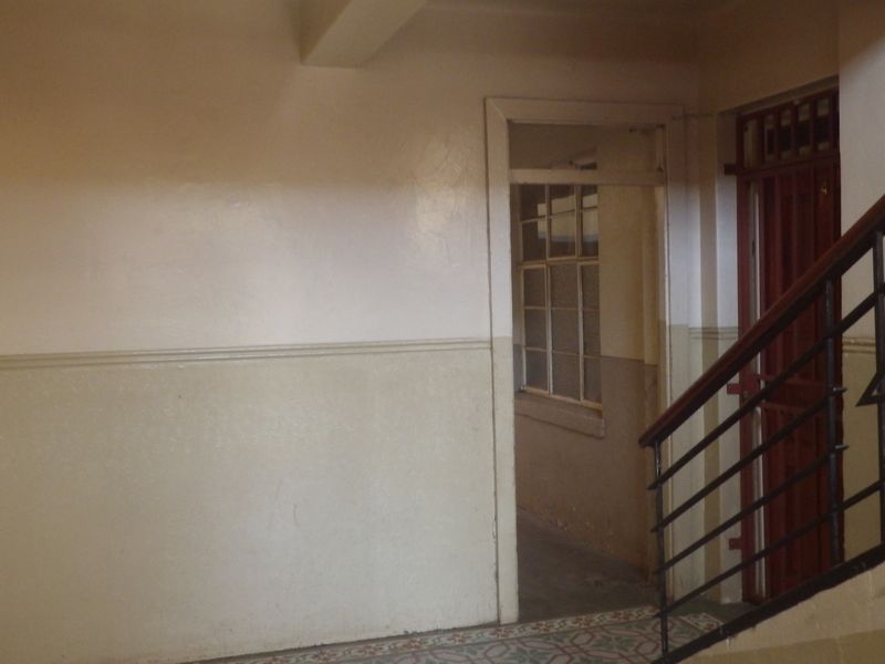 A functional apartment hallway featuring a metal security gate, staircase railing, and tiled flooring, showing signs of wear and dated finishes.