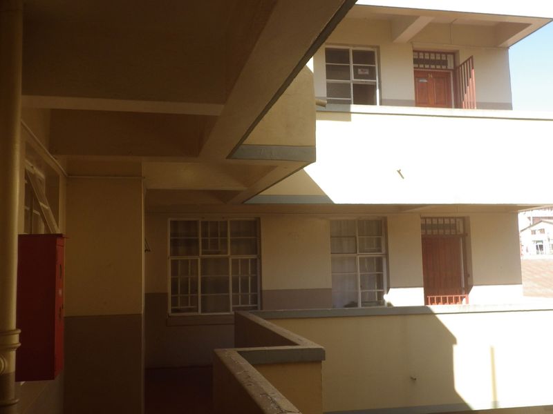 Exterior view of a multi-story flat complex featuring concrete walkways, external staircases, and fire safety equipment.