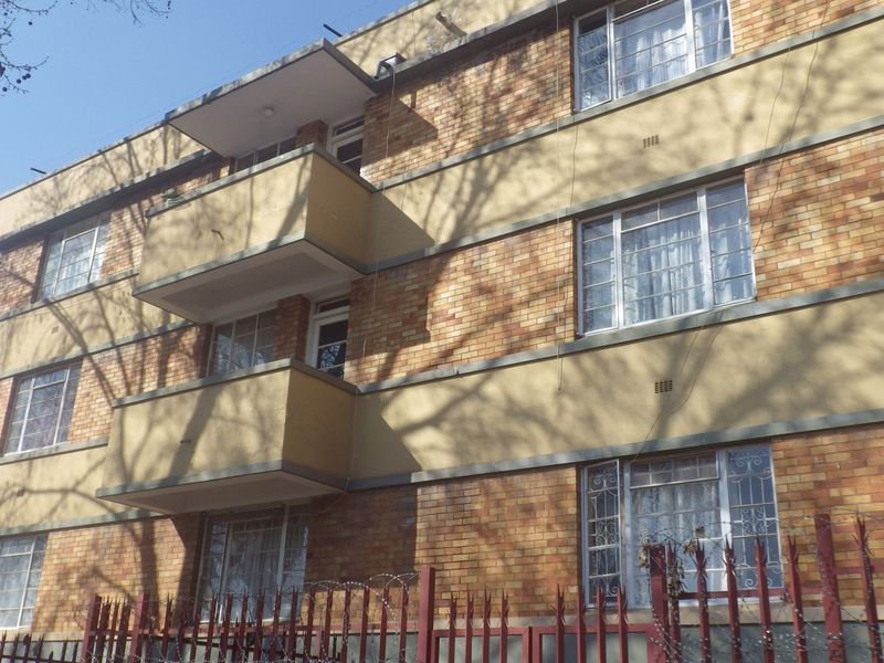 Exterior view of a multi-story brick apartment building featuring private balconies, security window bars, and a fenced perimeter with razor wire.