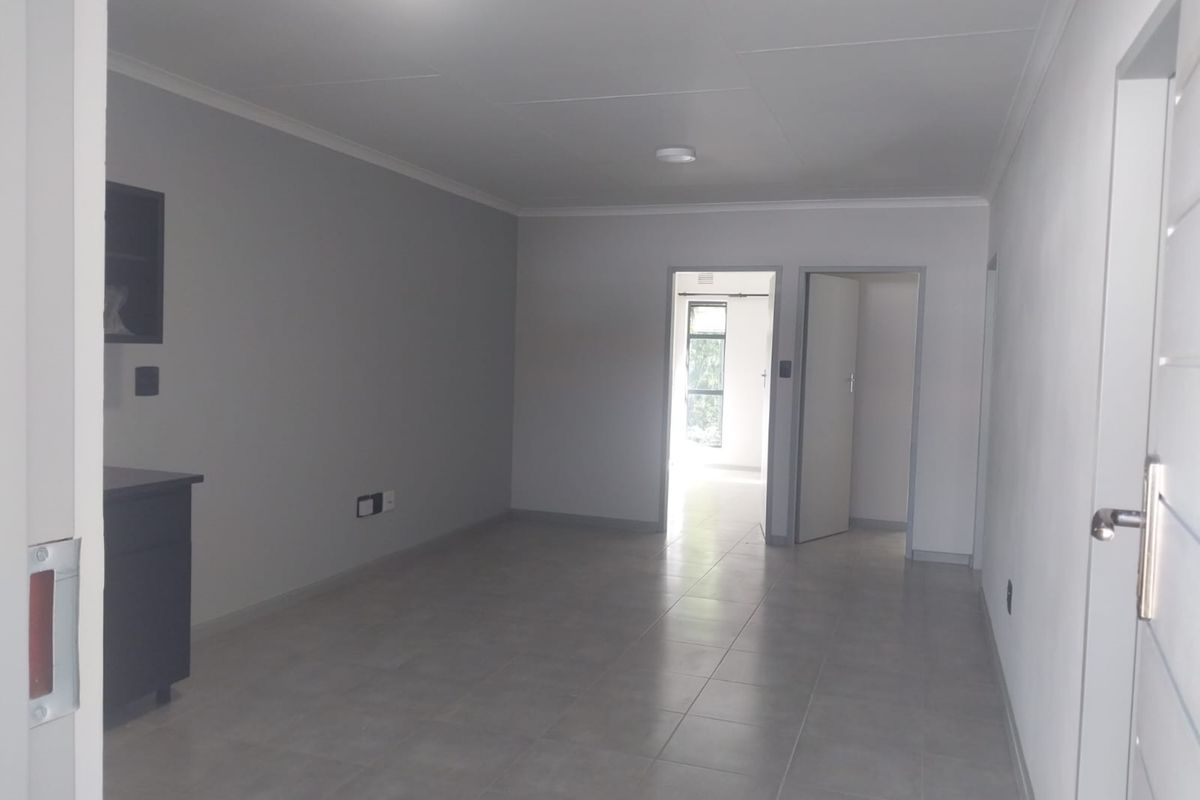 A bright, empty living area featuring neutral grey walls, tiled flooring, and coved ceilings, providing a clean and versatile space.