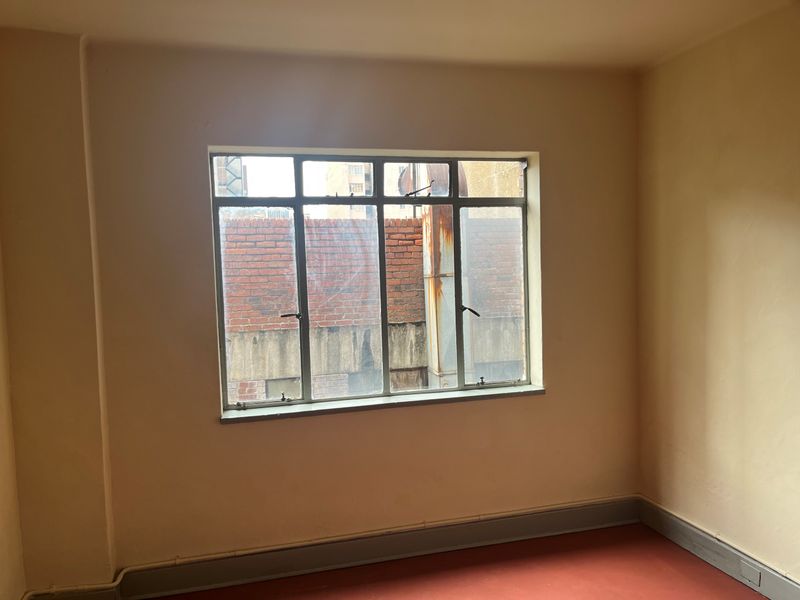 An empty bedroom featuring a metal-framed window and painted walls, offering a blank canvas for renovation or interior design updates.