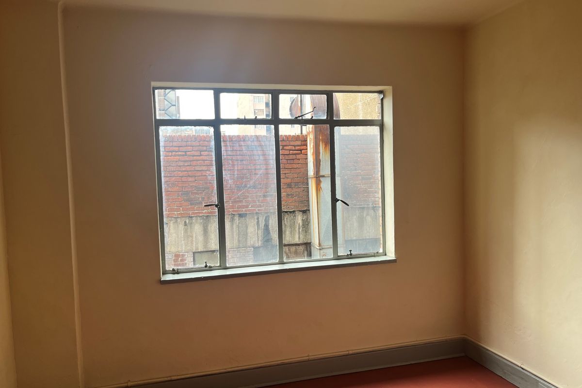 An empty bedroom featuring a metal-framed window and painted walls, offering a blank canvas for renovation or interior design updates.