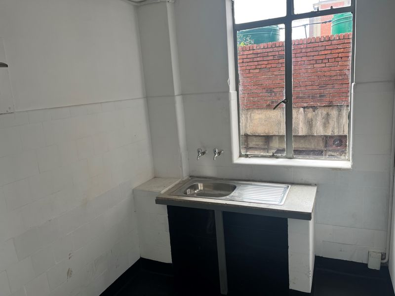 A functional laundry area featuring a stainless steel sink, tiled splashback, and a window overlooking an exterior brick wall.