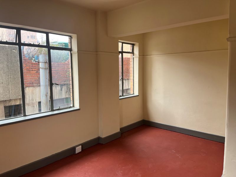 An empty bedroom featuring steel-framed windows, painted concrete flooring, and neutral wall finishes, offering a blank canvas for renovation or interior design.