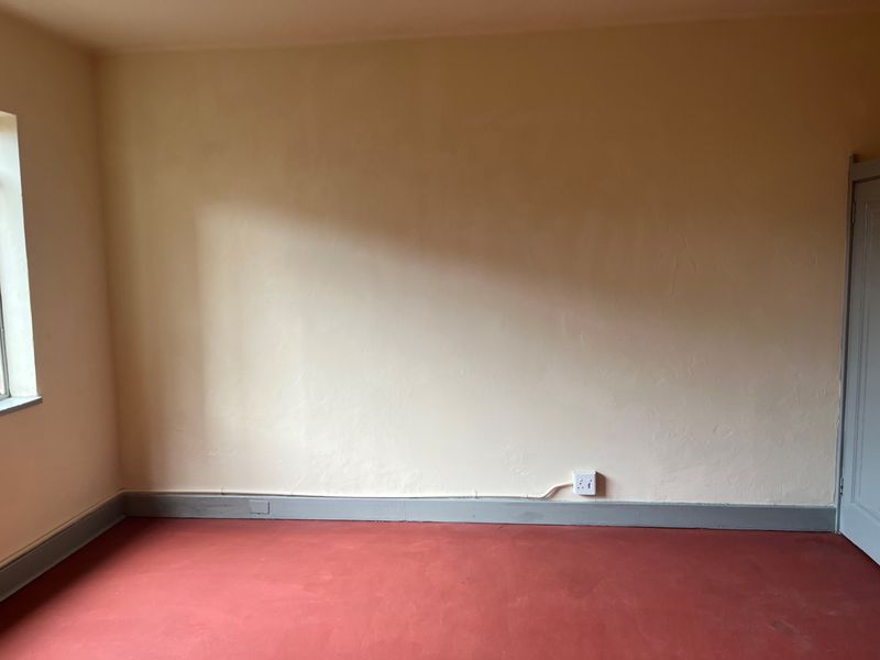 An empty bedroom featuring painted concrete flooring, neutral wall finishes, and a single window, providing a blank canvas for renovation or interior design updates.