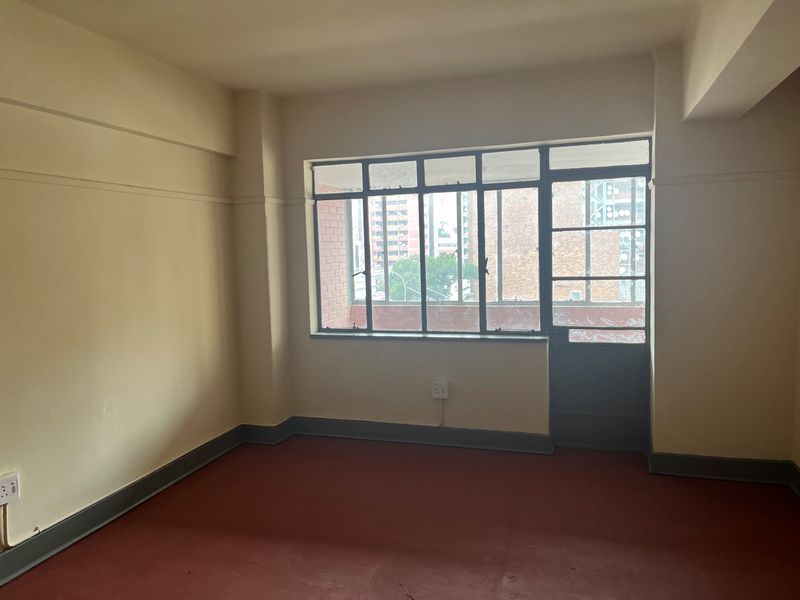 An empty bedroom featuring painted concrete flooring, a large multi-pane steel window, and a matching steel door leading to an exterior area.
