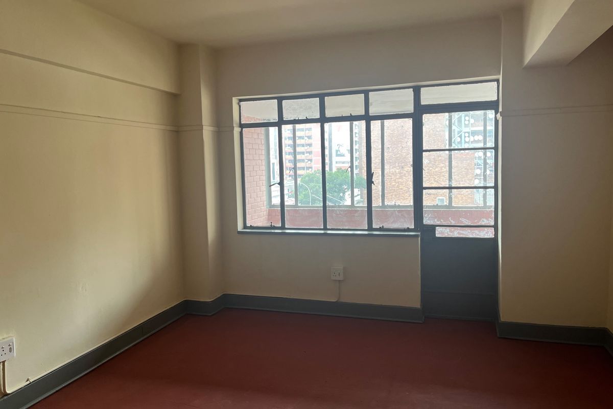 An empty bedroom featuring painted concrete flooring, a large multi-pane steel window, and a matching steel door leading to an exterior area.