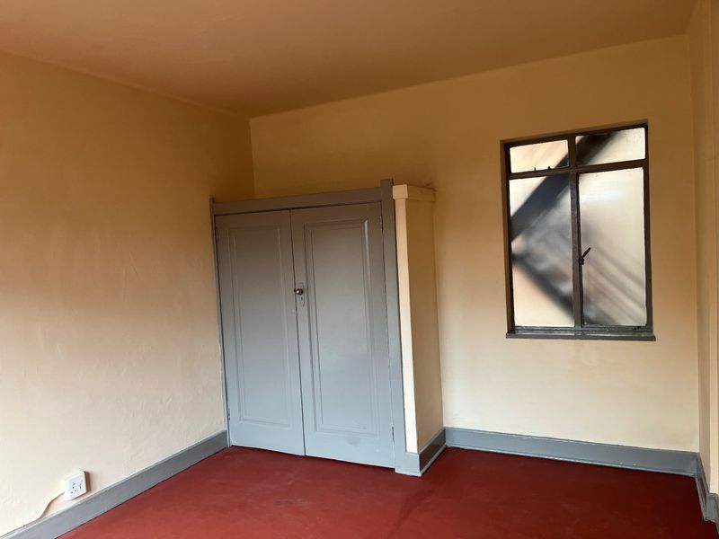 An empty bedroom featuring a built-in cupboard, steel-framed window, and painted flooring, offering a blank canvas for renovation or interior design updates.