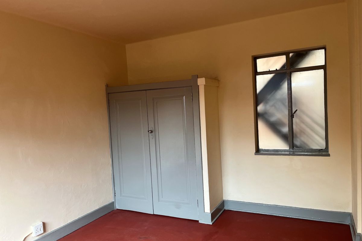 An empty bedroom featuring a built-in cupboard, steel-framed window, and painted flooring, offering a blank canvas for renovation or interior design updates.