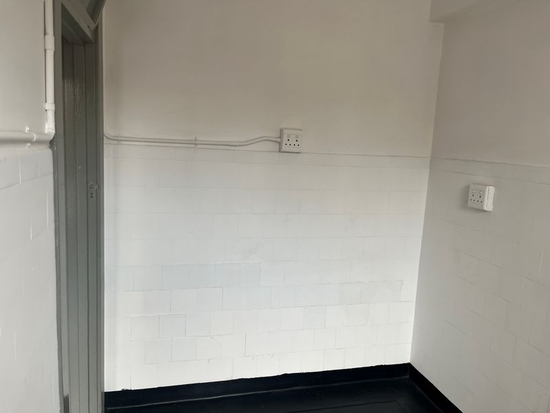 A functional hallway space featuring white tiled wall cladding, surface-mounted electrical points, and a painted door frame.
