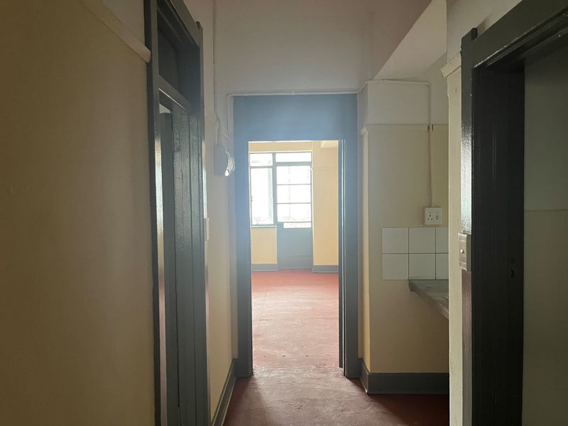 A functional hallway connecting interior spaces, featuring painted door frames, a small tiled splashback area, and direct access to an adjacent room.