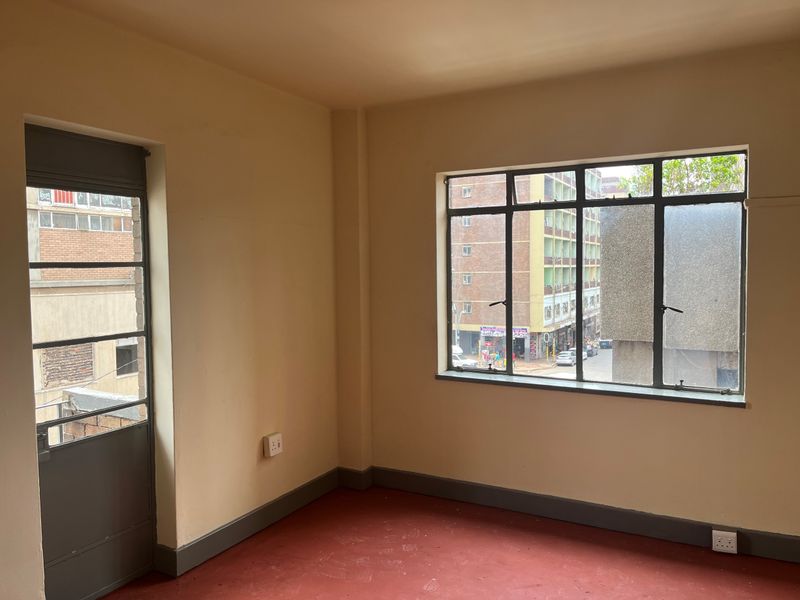An empty bedroom featuring steel-framed windows, a steel door, and painted concrete flooring, offering a blank canvas for renovation.