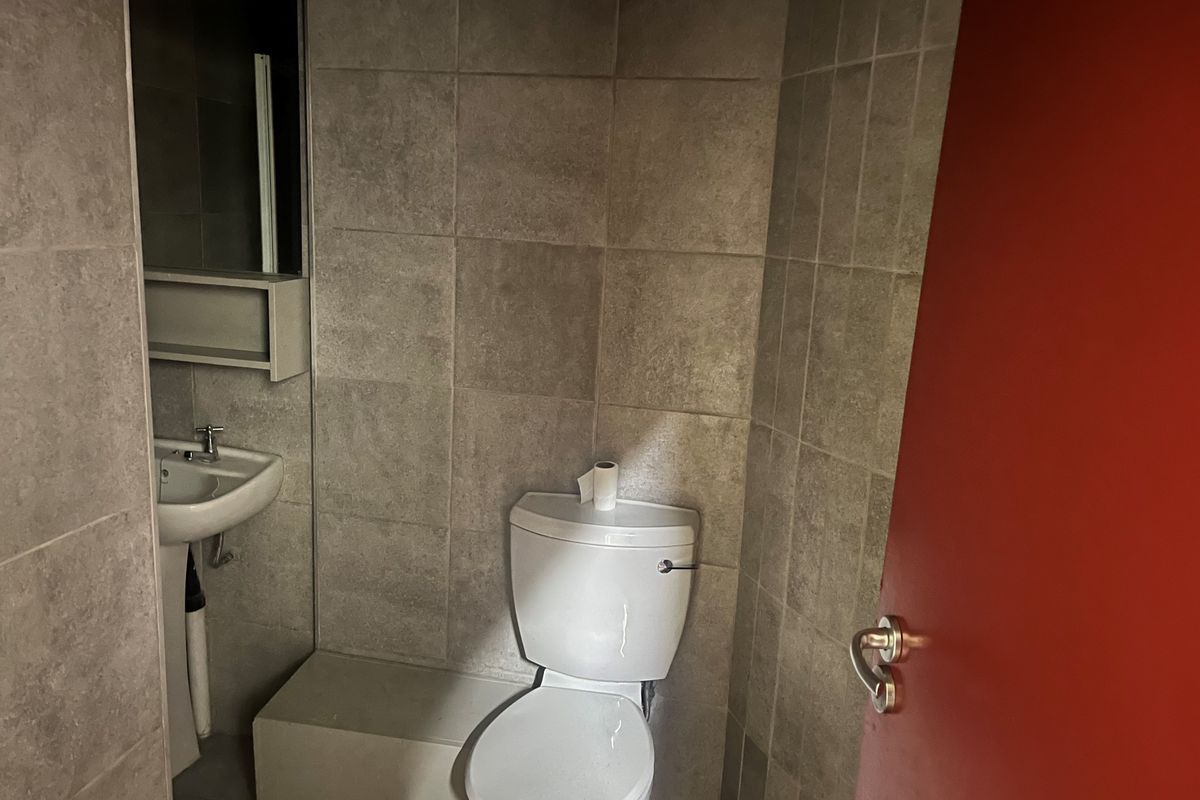 A compact bathroom featuring tiled walls and flooring, a pedestal basin, and a standard toilet.