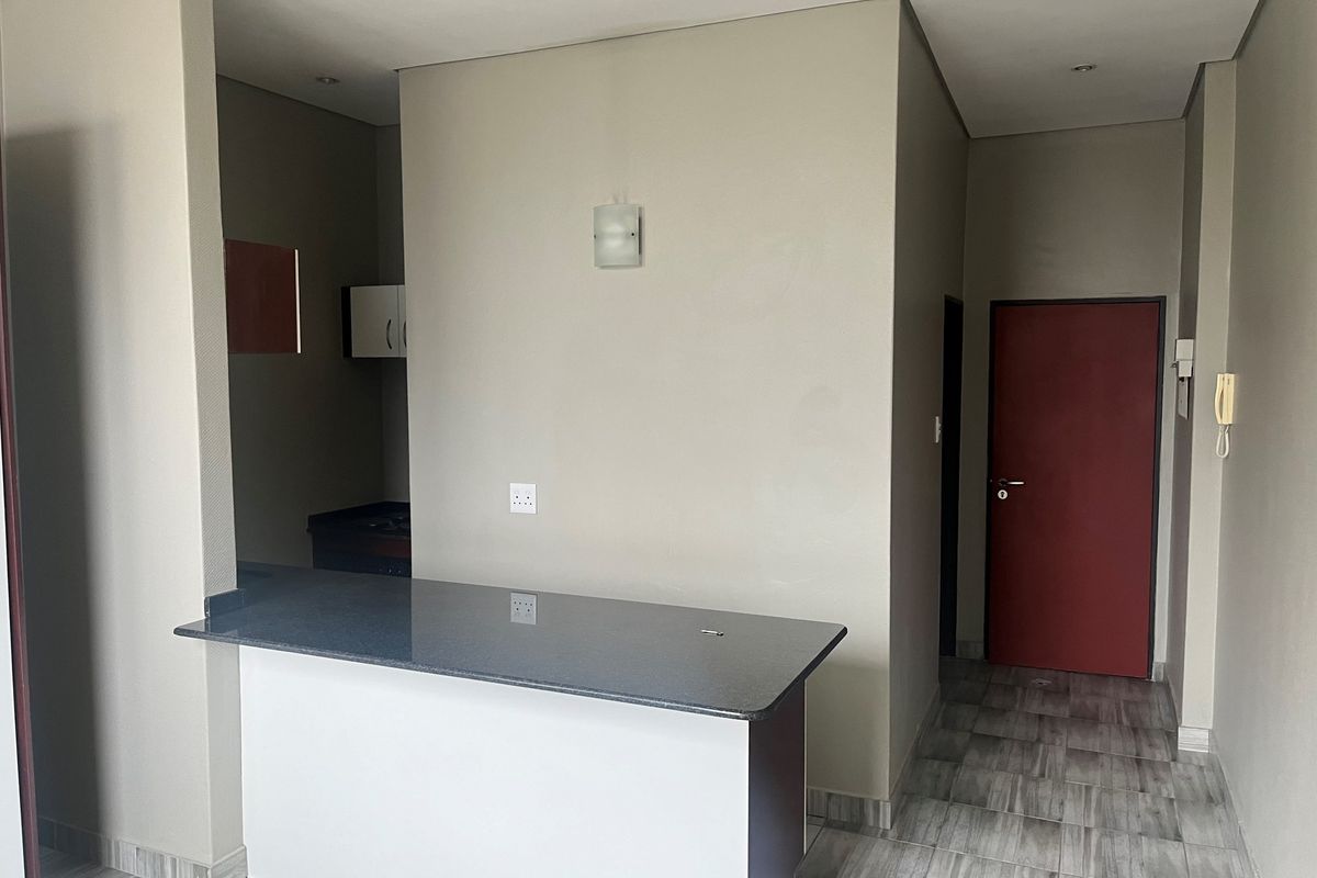 An open-plan living area featuring a granite breakfast counter, neutral wall finishes, and modern tiled flooring, leading to a separate kitchen and entrance.