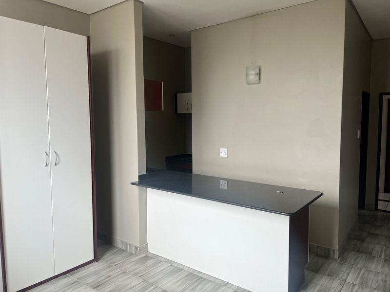Open plan living area featuring a breakfast bar with granite countertop, built-in storage cupboard, and neutral tiled flooring.