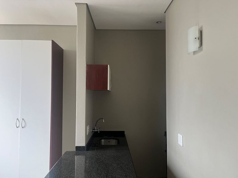 A compact scullery area featuring a granite countertop, undermount sink, and built-in cabinetry, providing a functional prep or wash-up space.
