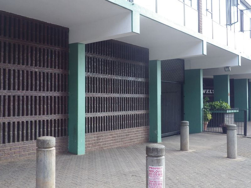 Exterior view of the building entrance featuring a brick screen wall, concrete pillars, and a paved walkway with security bollards.