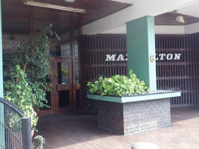 The entrance area of the apartment building features a paved walkway, a brick planter box, and a timber-framed doorway.
