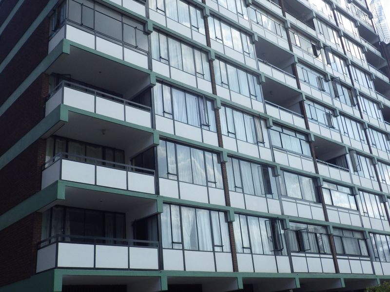 Exterior view of a multi-story apartment building featuring a repetitive facade with balconies and large sliding glass windows.