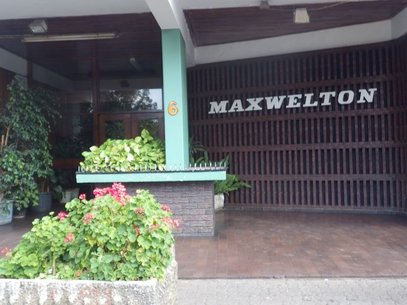 The entrance facade of Maxwelton apartment building, featuring a timber slat screen, brick planter box, and covered paved entryway.