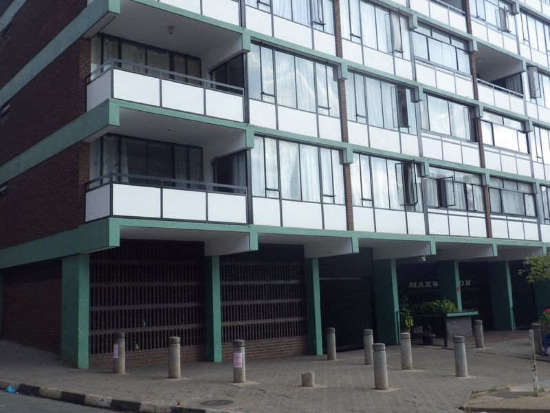 Exterior view of a multi-story apartment building featuring brick facade, private balconies with sliding glass doors, and ground-level concrete bollards.