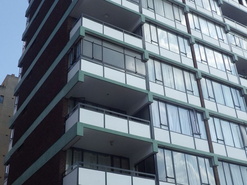 A multi-story residential apartment building featuring a brick facade, uniform balconies, and large windows throughout the exterior elevation.