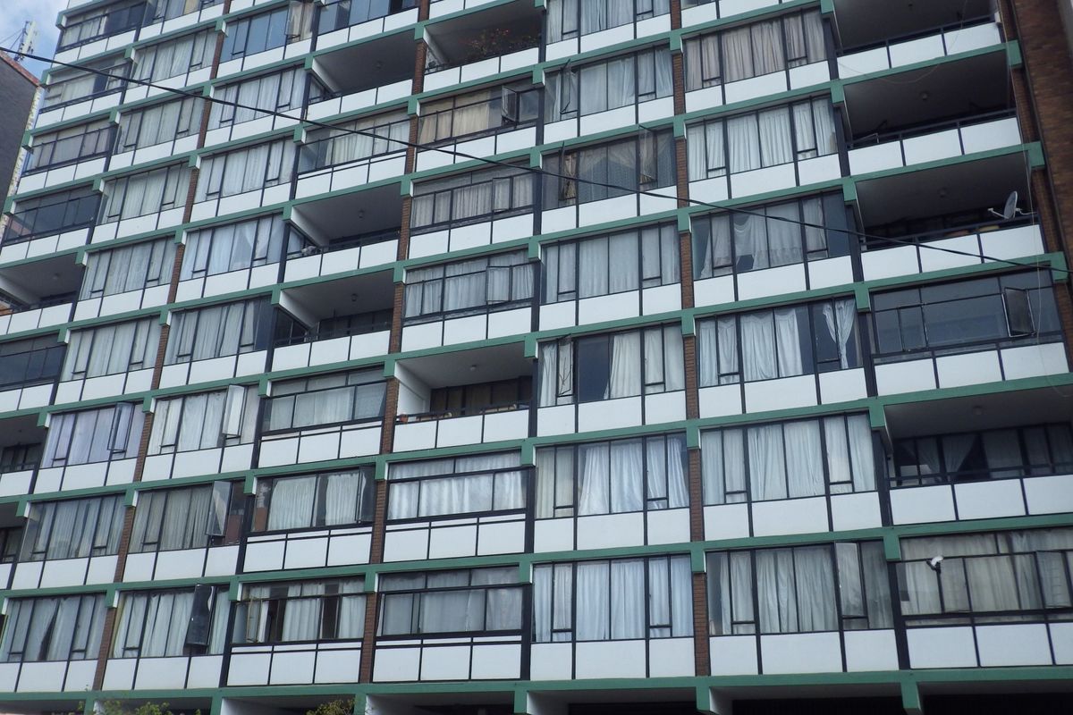 A multi-story apartment building facade featuring uniform balconies and large sliding glass windows across multiple levels.