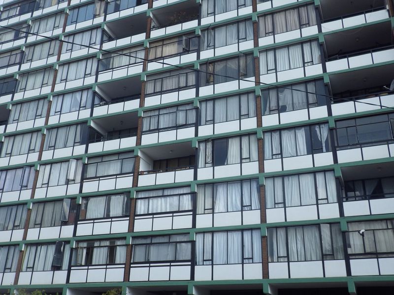 A multi-story apartment building facade featuring uniform balconies and large sliding glass windows across multiple levels.