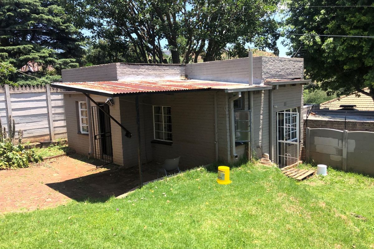 Rear view of a detached brick outbuilding featuring a corrugated iron roof, security gates, and steel window frames set within a garden area.